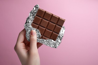 Woman holding delicious chocolate bar on pink background, closeup