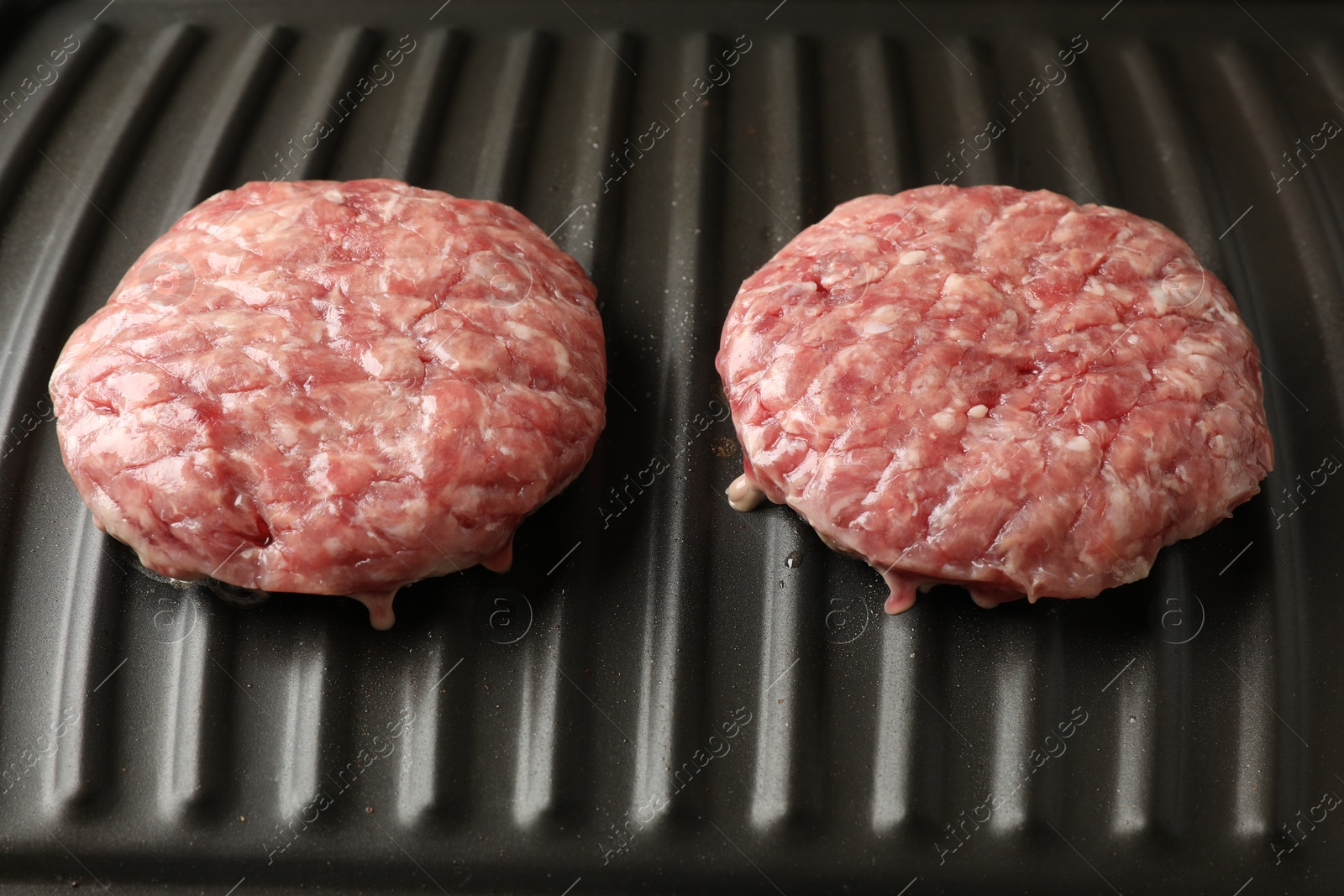 Photo of Fresh raw hamburger patties on electric grill, closeup