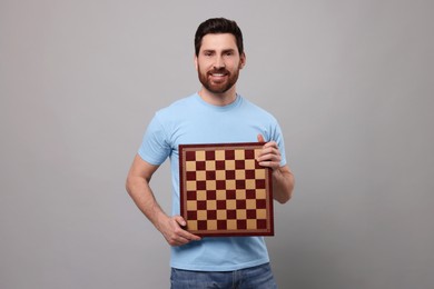 Smiling man holding chessboard on light grey background