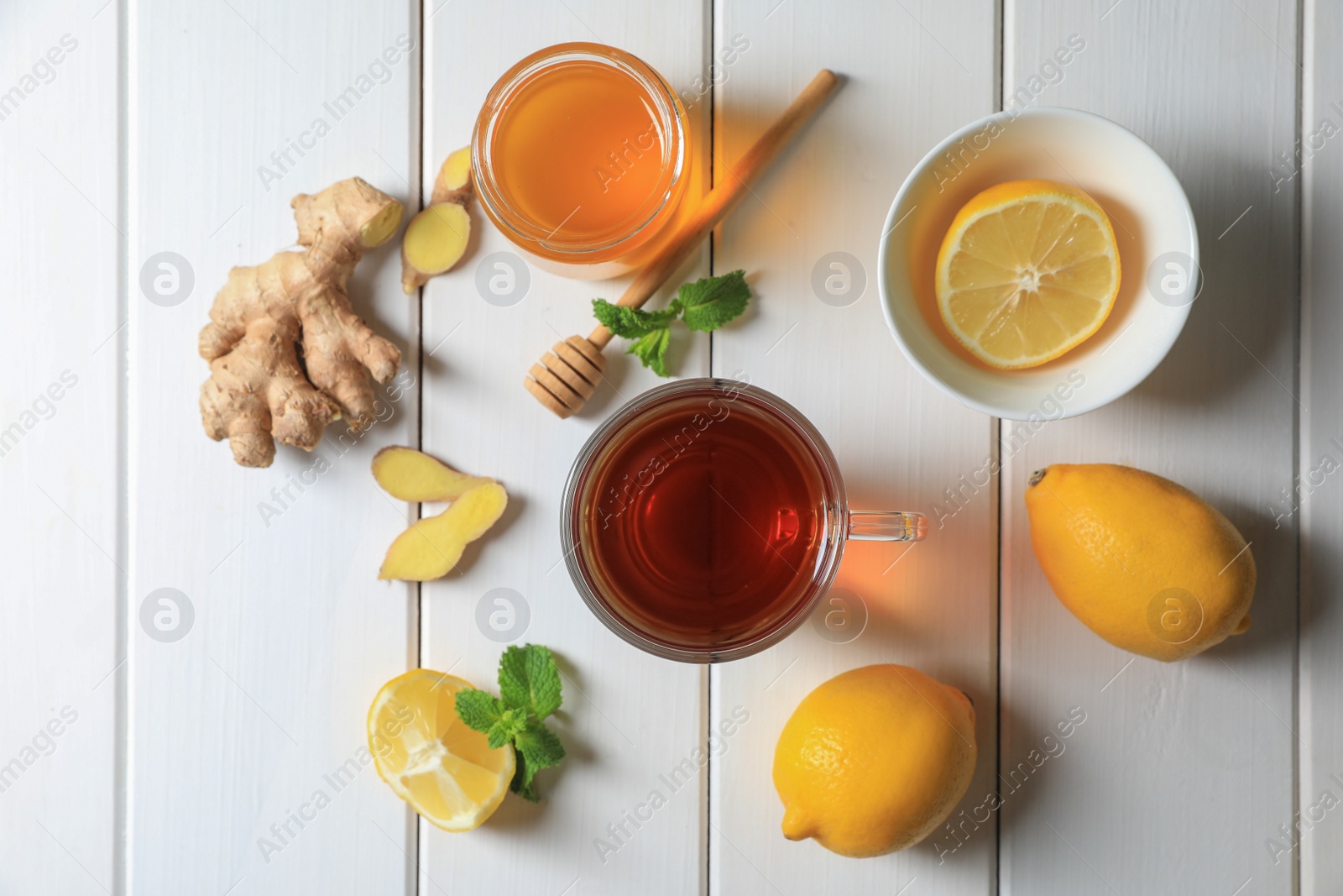 Photo of Cup of delicious ginger tea, honey and lemons on white wooden table, flat lay