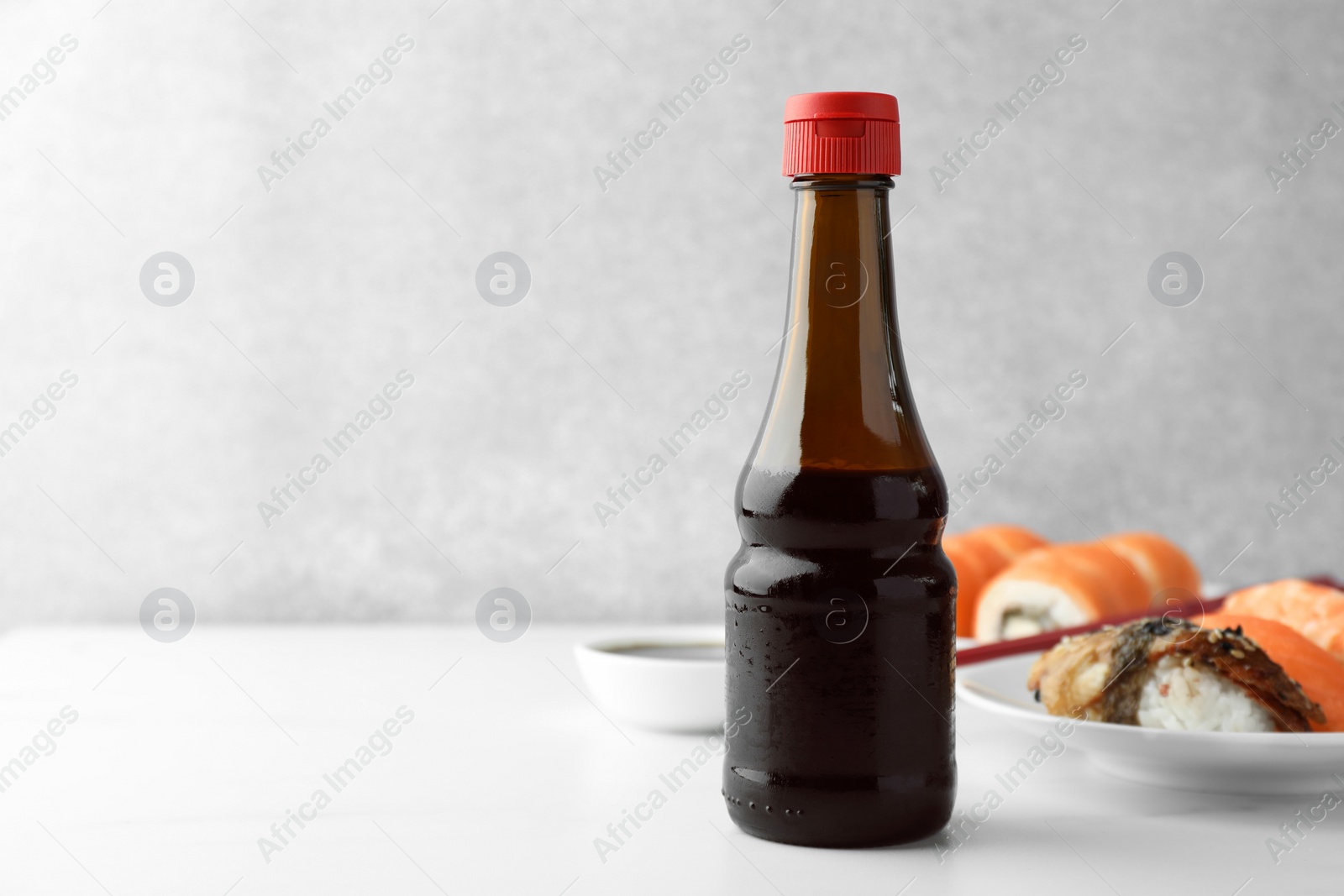 Photo of Tasty soy sauce and different types of sushi on white table. Space for text