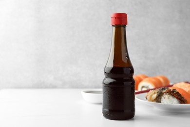 Tasty soy sauce and different types of sushi on white table. Space for text