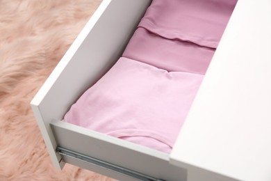 Folded pink clothes in white chest of drawers indoors, closeup