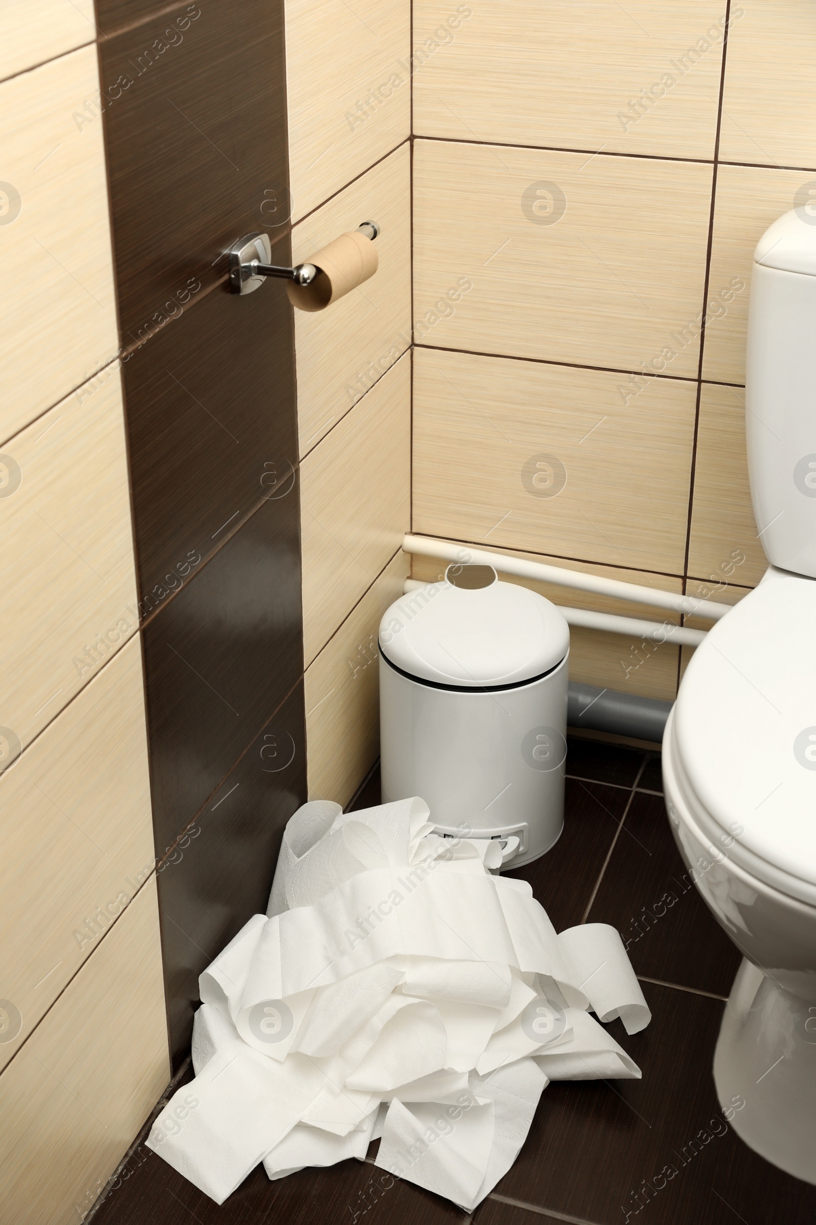 Photo of Soft toilet paper unrolled from holder on floor in bathroom