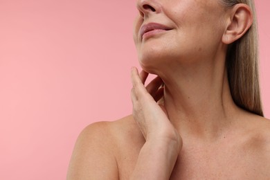 Mature woman touching her neck on pink background, closeup. Space for text