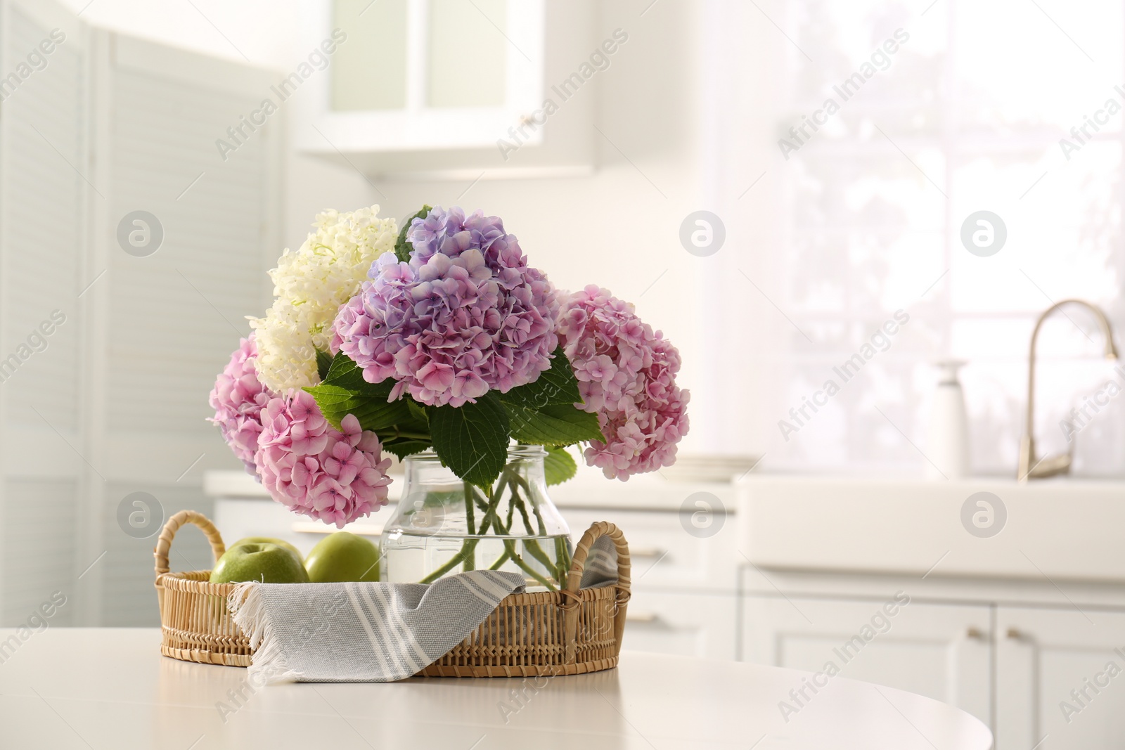 Photo of Bouquet of beautiful hydrangea flowers and apples on table in kitchen, space for text. Interior design