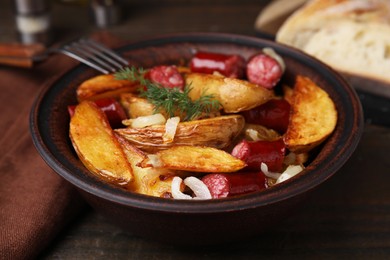 Photo of Delicious baked potato with thin dry smoked sausages, onion and dill in bowl on wooden table, closeup