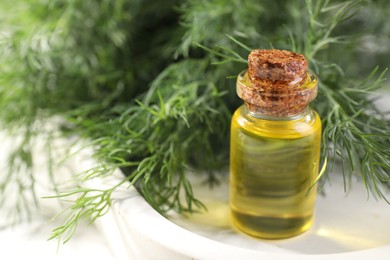 Bottle of essential oil and fresh dill on light tray, closeup