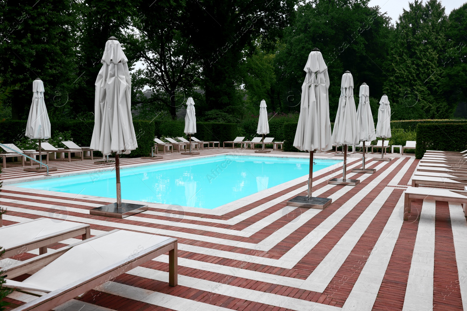 Photo of Many sunbeds and umbrellas near outdoor swimming pool