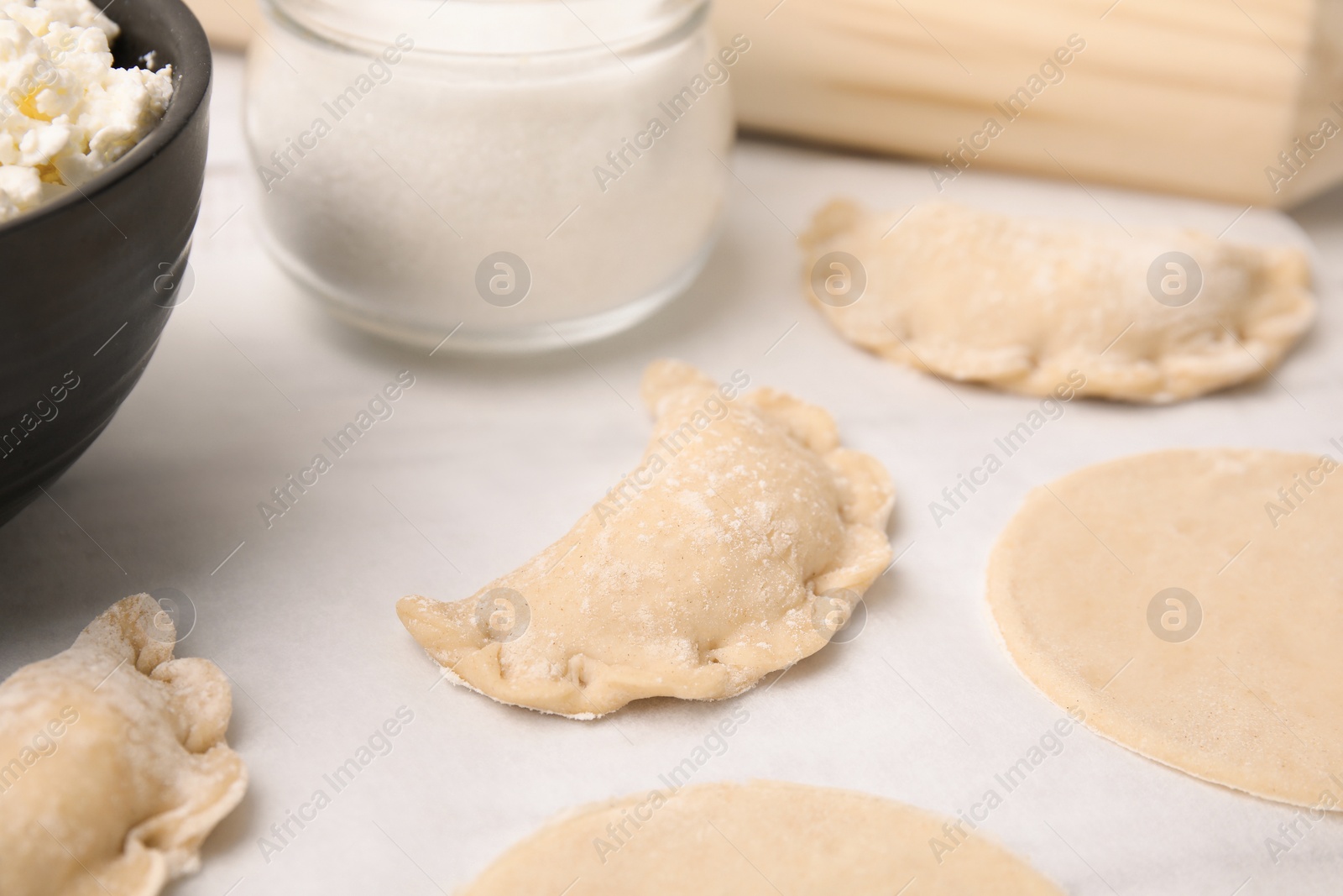 Photo of Process of making dumplings (varenyky) with cottage cheese. Raw dough and ingredients on white table, closeup