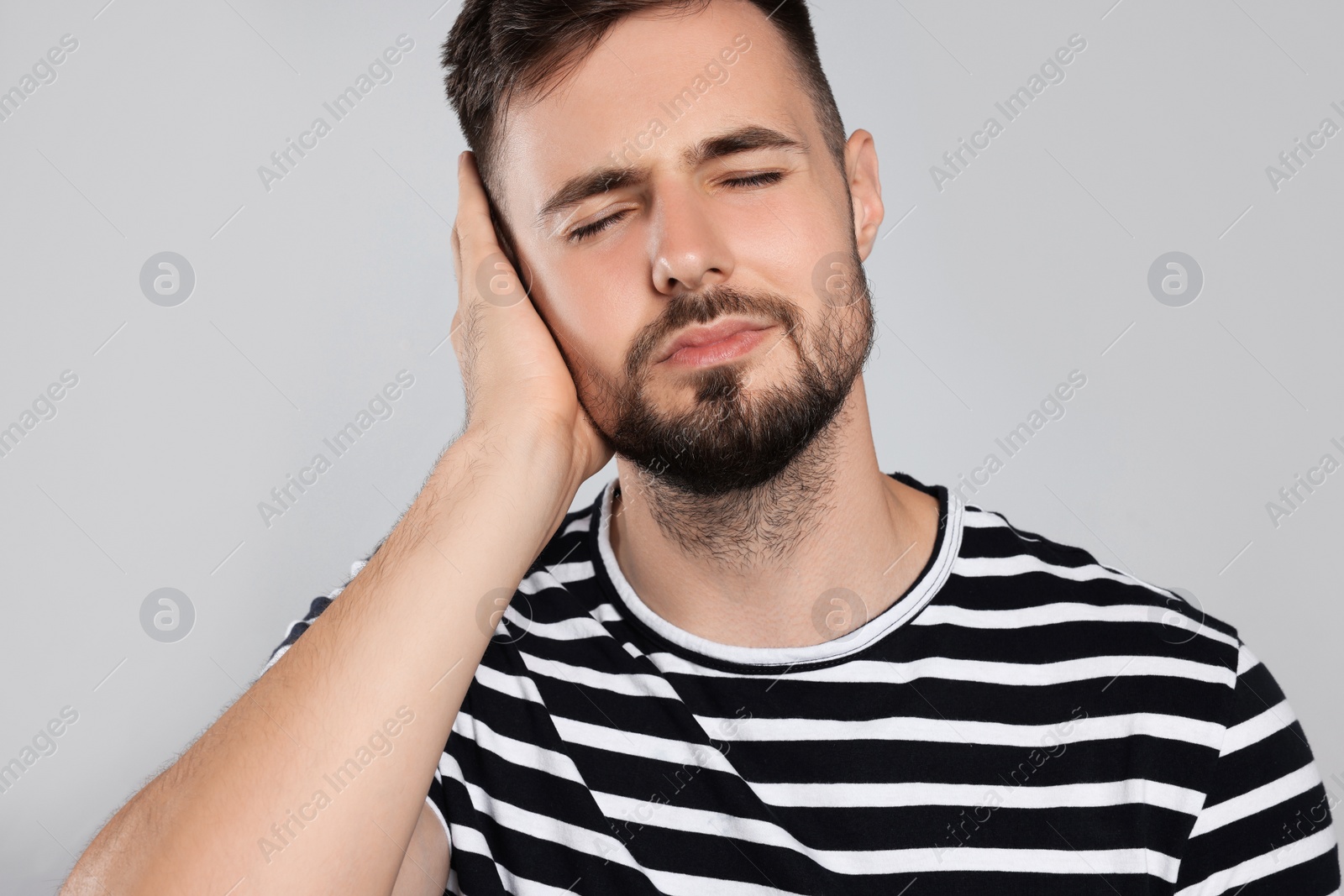Photo of Young man suffering from ear pain on light grey background