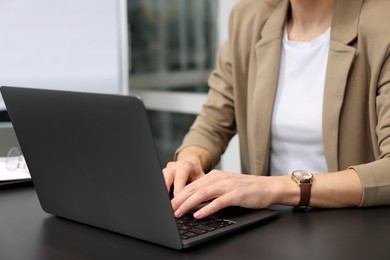 Woman working on laptop at black desk in office, closeup