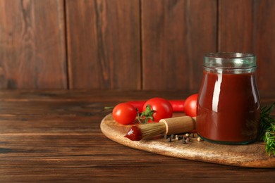 Photo of Tasty barbecue sauce in glass jar, brush and ingredients on wooden table, closeup. Space for text