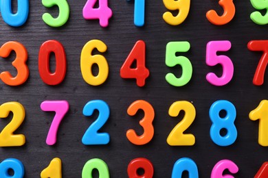 Photo of Colorful numbers on dark wooden school desk, flat lay