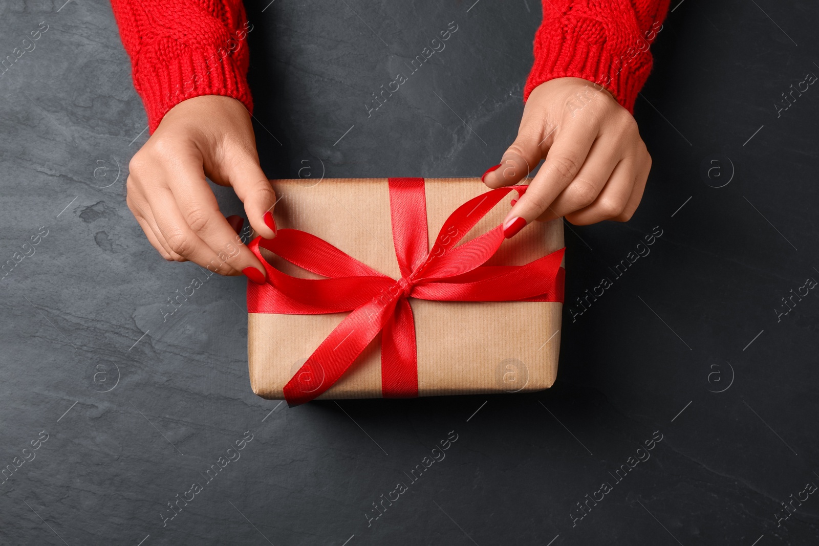 Photo of Christmas present. Woman with gift box at black table, top view