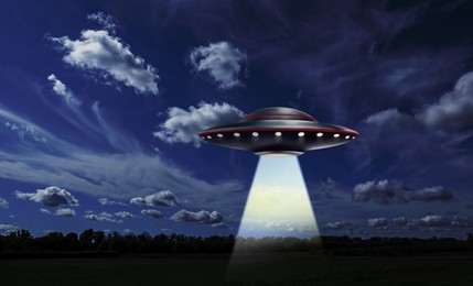 Image of UFO. Alien spaceship emitting light beam over meadow