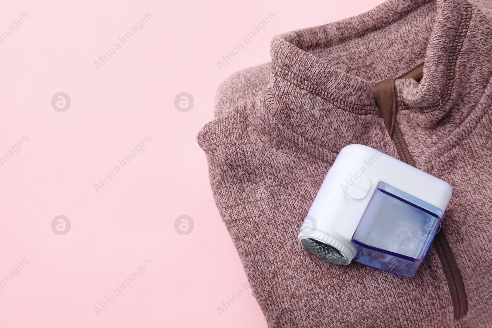 Photo of Fabric shaver and sweater on pink background, top view. Space for text