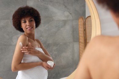 Photo of Beautiful young woman applying body cream onto arm indoors