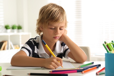Photo of Bored little boy doing homework at table indoors