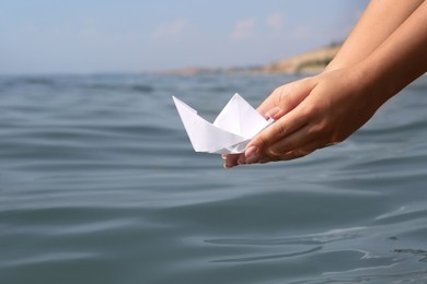 Photo of Woman holding white paper boat near sea, closeup