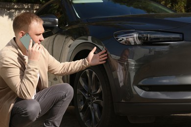 Photo of Man talking on phone near car with scratch outdoors