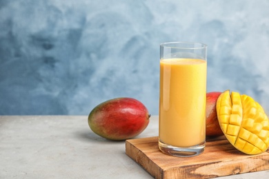 Glass of fresh mango drink and fruits on table against color background. Space for text