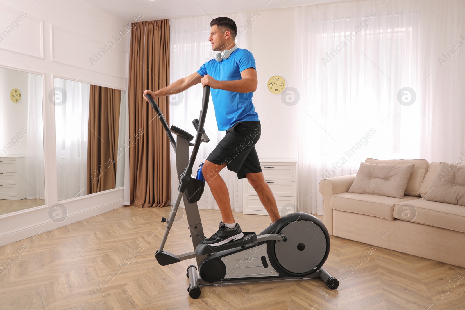 Photo of Man with headphones using modern elliptical machine at home