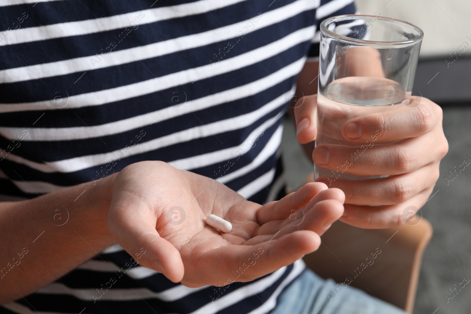 Photo of Man with glass of water and pill on blurred background, closeup