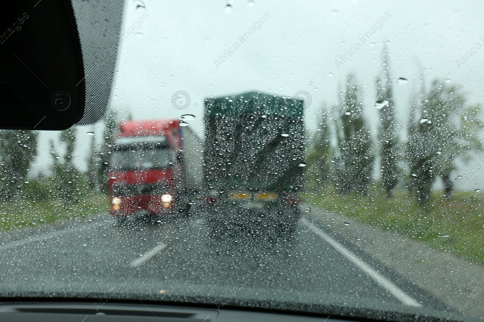 Photo of Blurred view of country road through wet car window. Rainy weather