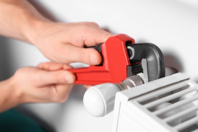 Photo of Professional plumber using adjustable wrench for installing new heating radiator, closeup