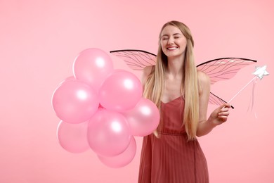 Photo of Beautiful girl in fairy costume with wings, magic wand and balloons on pink background