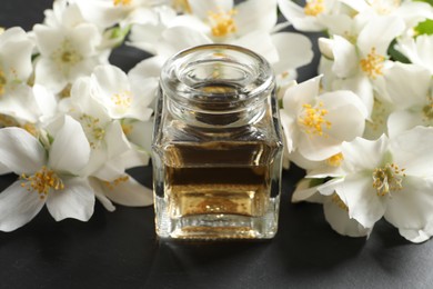 Photo of Jasmine essential oil and fresh flowers on dark grey table