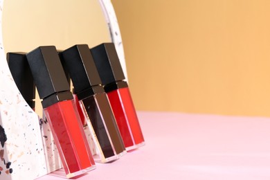 Photo of Different lip glosses and mirror on color background, closeup. Space for text