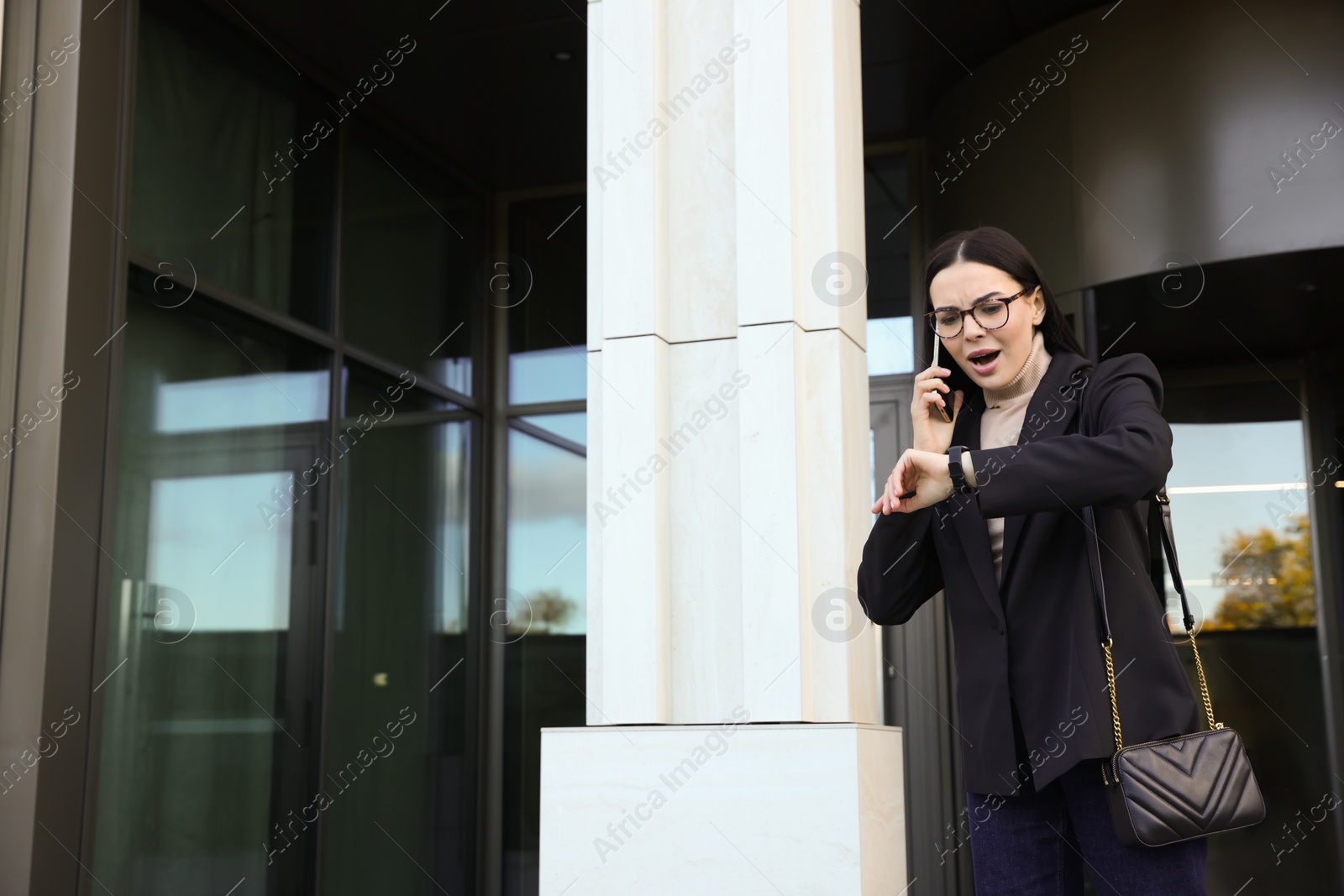 Photo of Emotional woman checking time while talking on smartphone outdoors. Being late concept