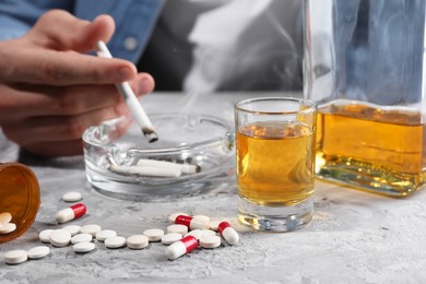 Photo of Alcohol and drug addiction. Man with smoldering cigarettes, whiskey and pills at grey textured table, closeup