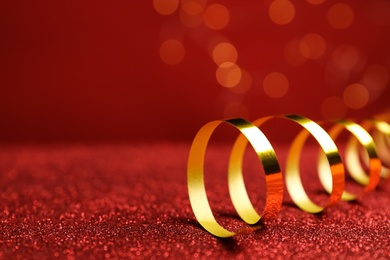 Photo of Shiny golden serpentine streamer on red table against blurred lights, closeup. Space for text