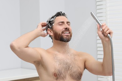 Happy man washing his hair with shampoo in shower