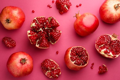 Photo of Whole and cut fresh pomegranates on pink background, flat lay