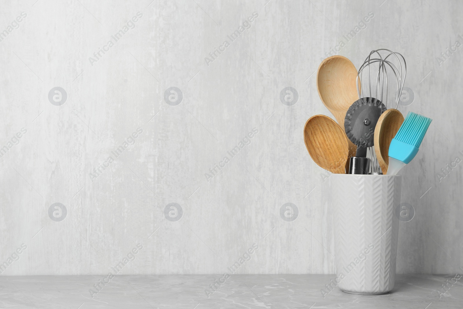 Photo of Holder with kitchen utensils on grey table against light background. Space for text