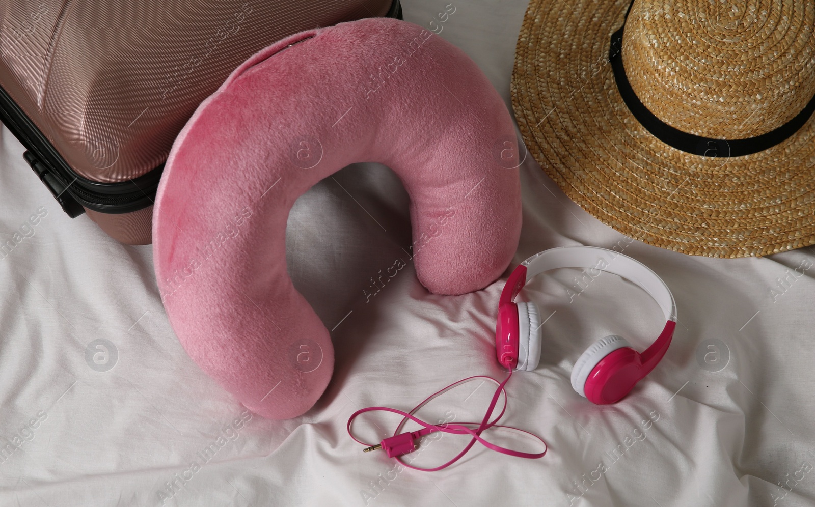 Photo of Pink travel pillow, suitcase, hat and headphones on bed