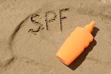 Abbreviation SPF written on sand and blank bottle of sunscreen at beach, above view
