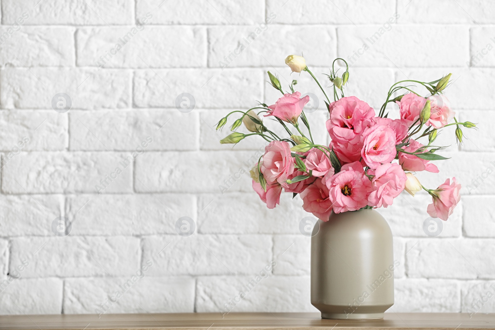 Photo of Vase with beautiful flowers on table against brick wall, space for text