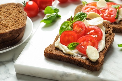 Photo of Toast bread with cherry tomatoes and mozzarella cheese on marble board, closeup