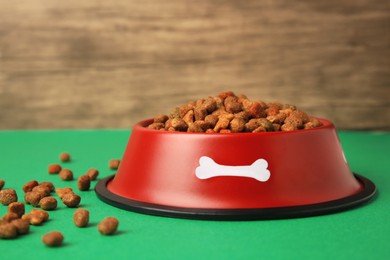 Photo of Dry pet food in feeding bowl on green background, closeup