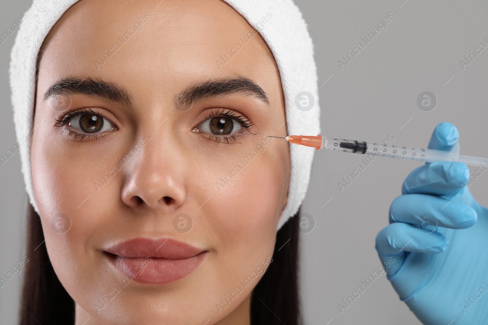 Photo of Doctor giving facial injection to young woman on light grey background, closeup. Cosmetic surgery