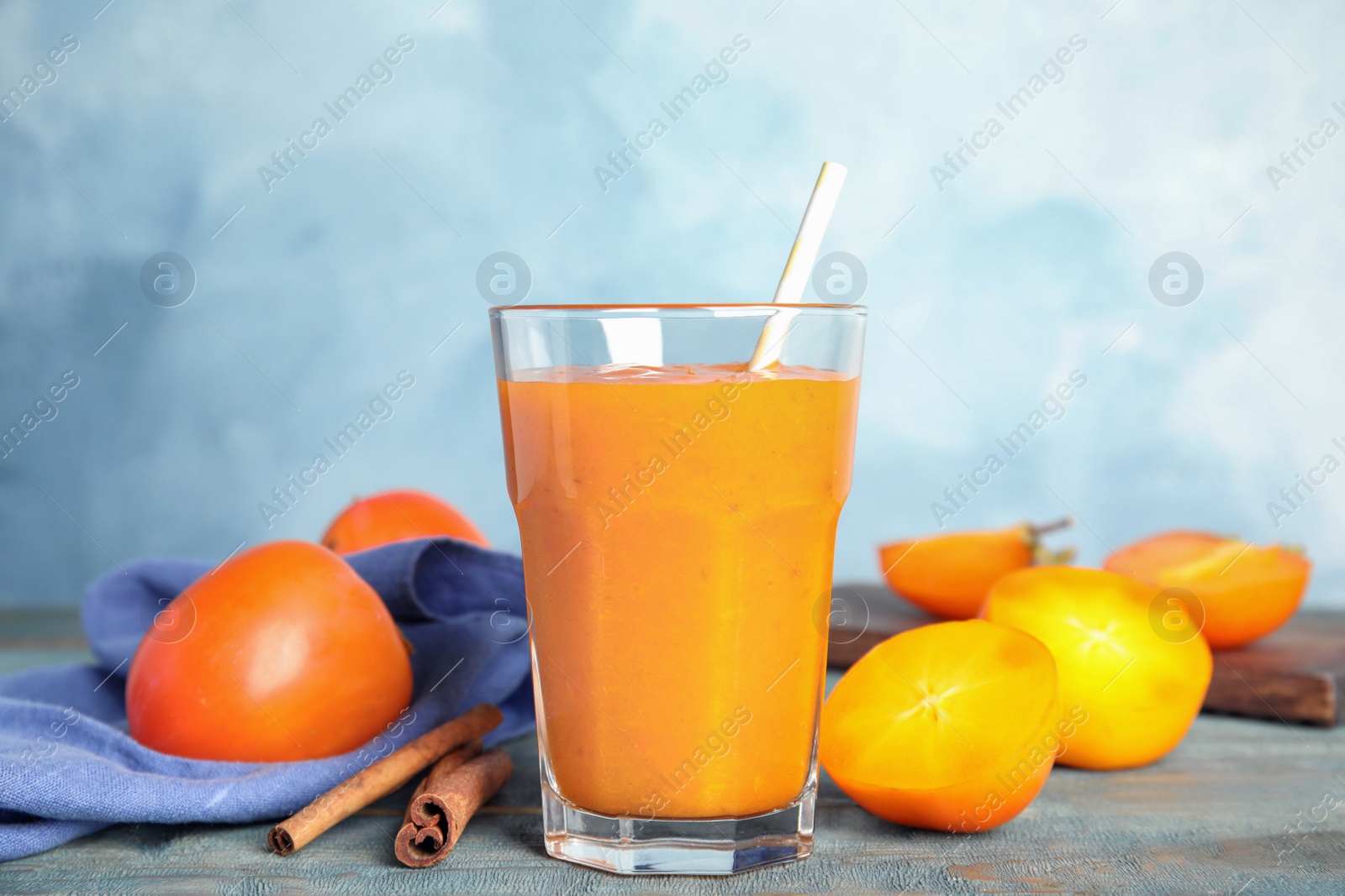 Photo of Tasty persimmon smoothie with straw and cinnamon on wooden table against light blue background