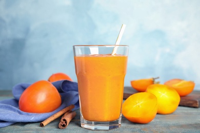 Photo of Tasty persimmon smoothie with straw and cinnamon on wooden table against light blue background