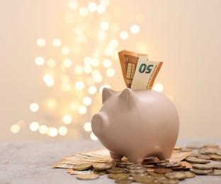 Piggy bank with euro banknote and coins on grey table against blurred lights