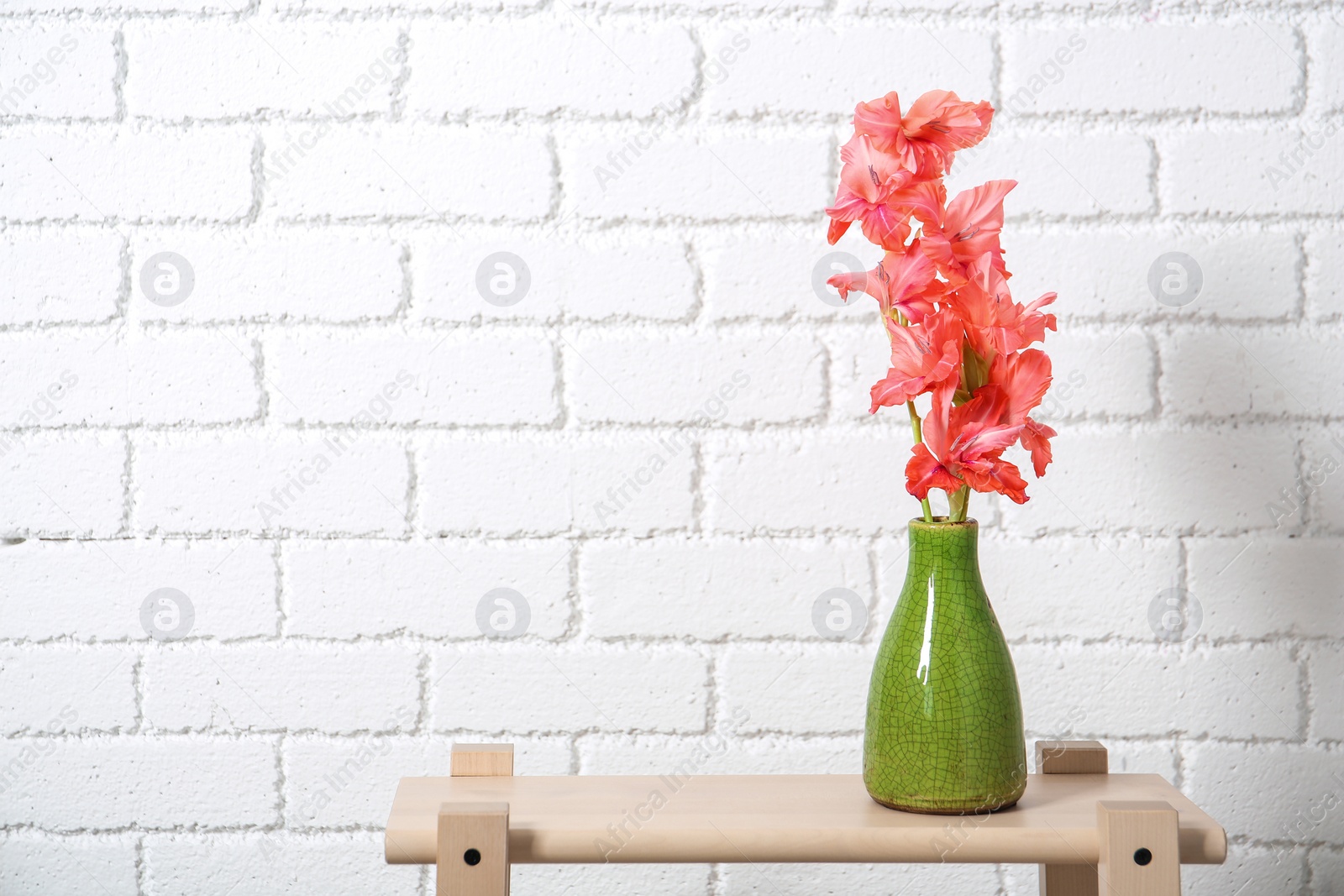 Photo of Vase with beautiful gladiolus flowers on table against brick wall