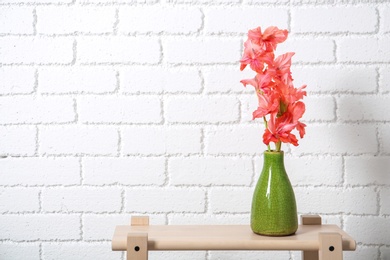 Photo of Vase with beautiful gladiolus flowers on table against brick wall